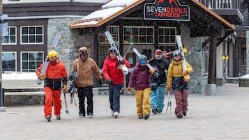 A group of people with skis and ski poles walking in front of a building with a sign that reads 'SEVEN DEVILS TAPHOUSE'.