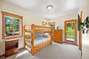 Ein Schlafzimmer mit Etagenbett, einem Holzschrank und einem Fenster mit Blick auf Grünflächen.