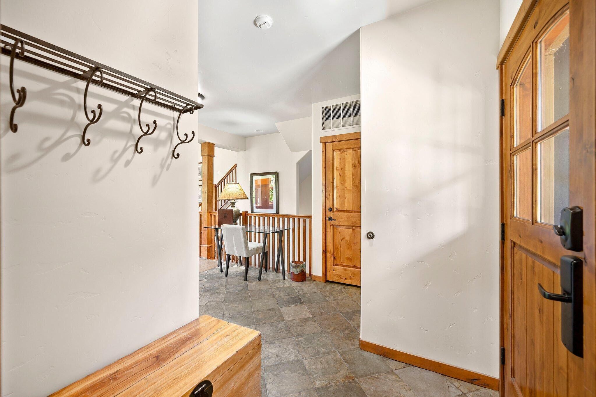 A hallway with a wooden bench, a coat rack, a dining area with a table and chairs, and a wooden door.