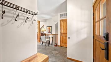 A hallway with a wooden bench, a coat rack, a dining area with a table and chairs, and a wooden door.