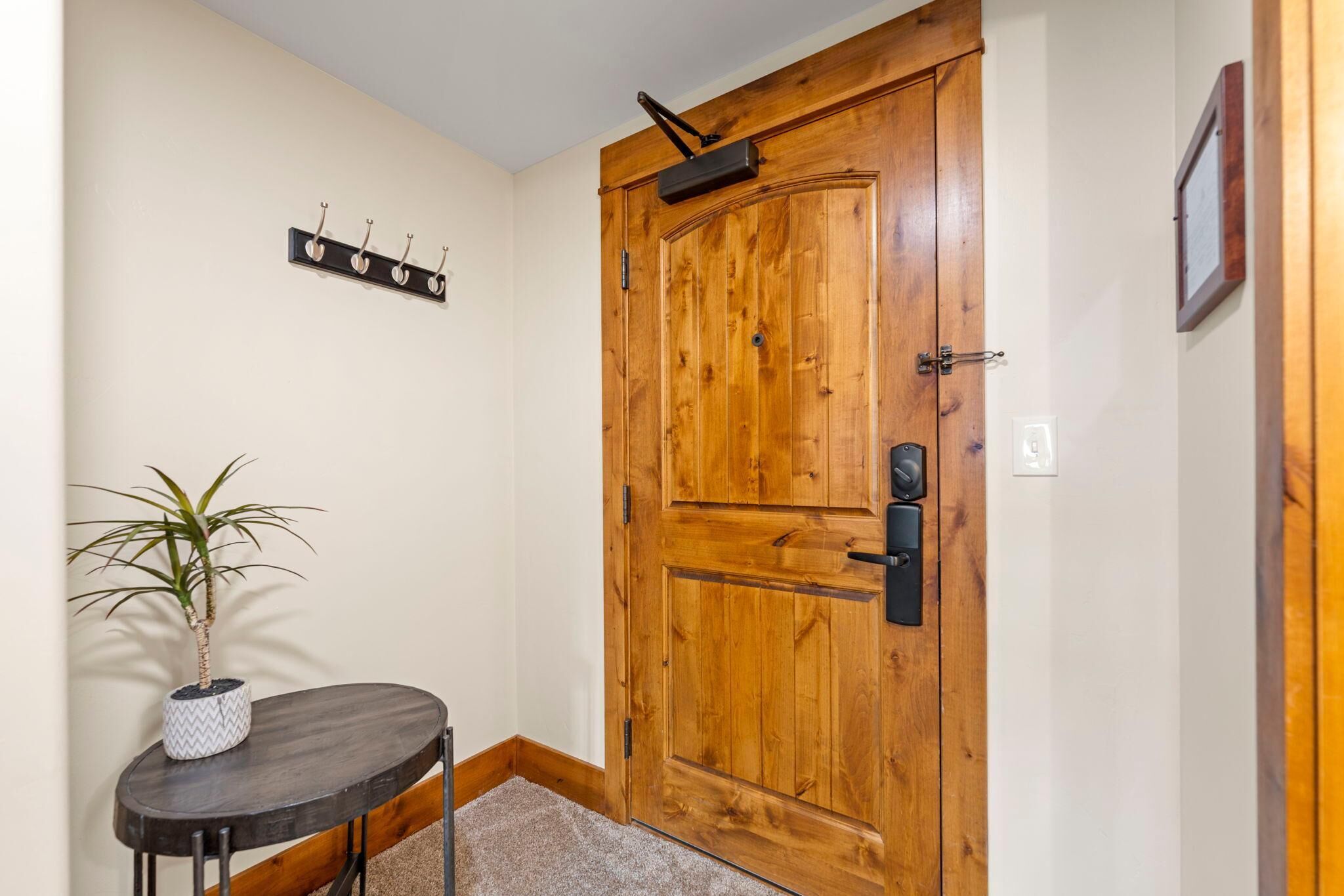 A wooden door with a handle and a keyhole, a small table with a potted plant, and a wall-mounted coat rack with hooks.