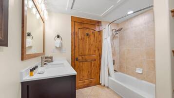 A bathroom with a wooden door, a white sink, a mirror, and a shower area.