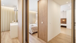 Una habitación de hotel moderna con piso de madera, una cama con ropa blanca, una mesita de noche y un espejo.