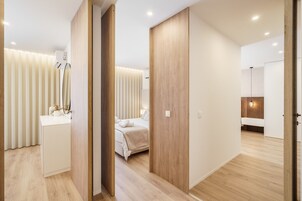 A modern hotel room with a wooden floor, a bed with white bedding, a bedside table, and a mirror.