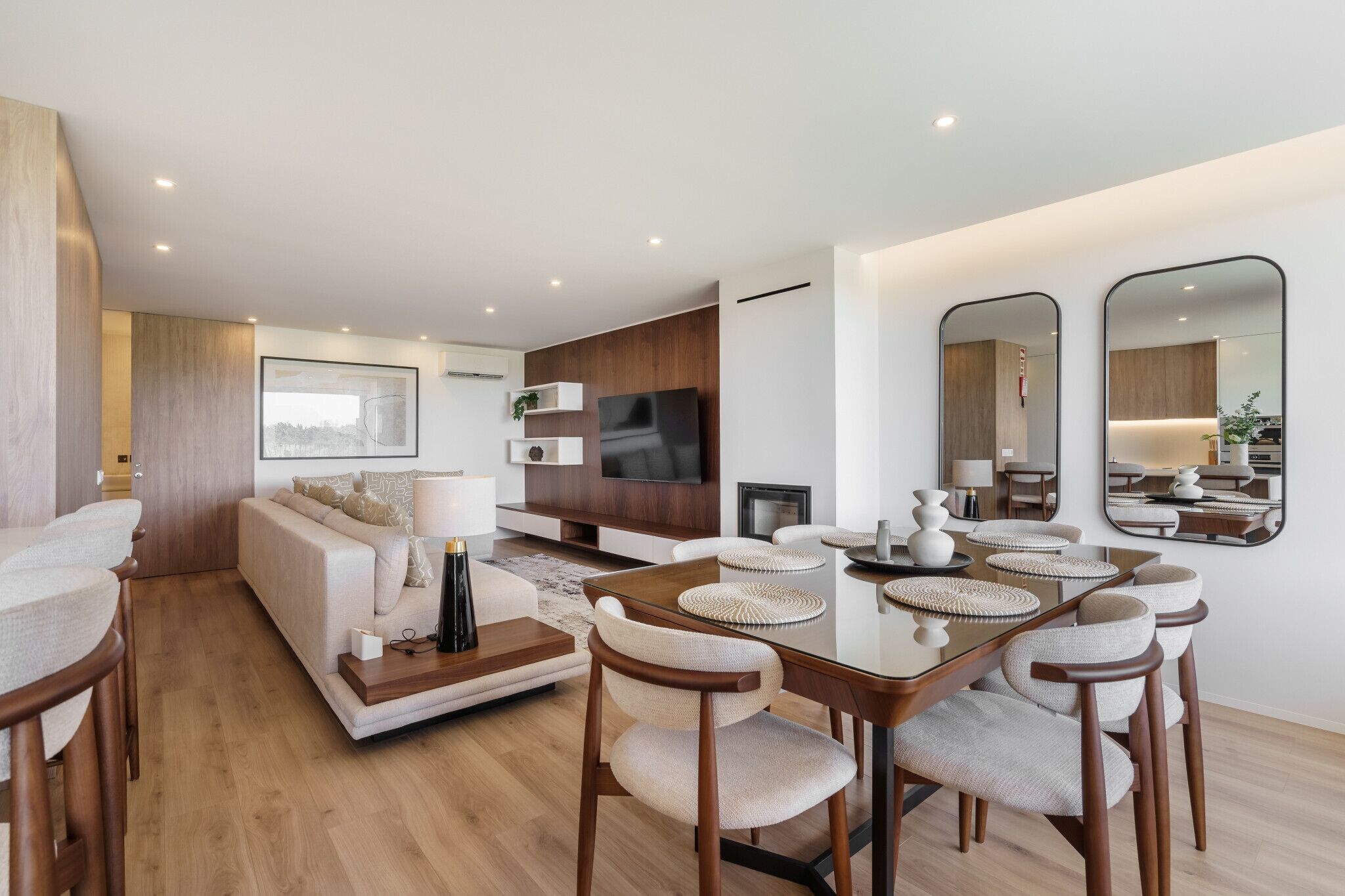 Uma sala de estar moderna com sofá, televisão, mesa de jantar, cadeiras e um espelho grande.