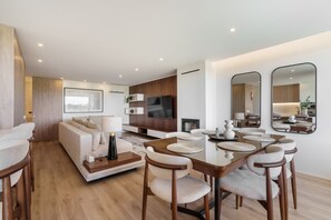 Una sala moderna con sofá, televisor, mesa de comedor, sillas y un espejo grande.