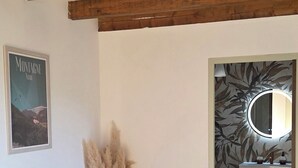 Une pièce avec des poutres en bois, un vase contenant de l’herbe des pampas, une affiche et un miroir orné d’un papier peint à motifs.