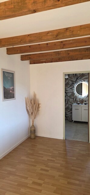 A room with wooden beams, a vase with pampas grass, a poster, and a mirror with patterned wallpaper.