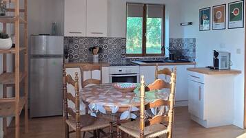 Eine Küche mit Holzbalken, einem Esstisch mit Stühlen, einem Kühlschrank und einem Fenster.