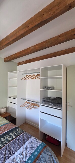 A bedroom with a wardrobe, a bed with patterned bedding, and wooden beams on the ceiling.