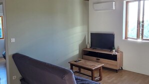 Une pièce avec un canapé, un téléviseur posé sur un meuble, des poutres en bois au plafond et une fenêtre.