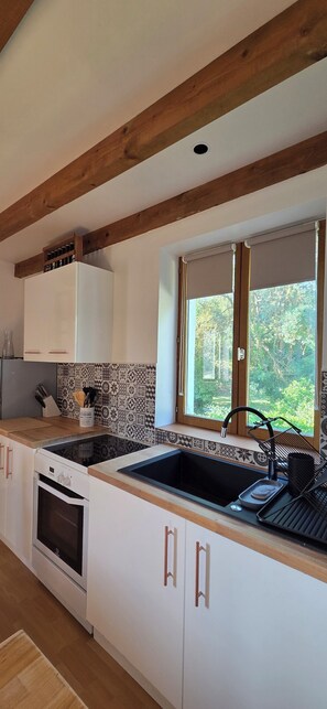 A kitchen with a wooden ceiling, white cabinets, a built-in oven, a sink, and a window with a view of greenery.
