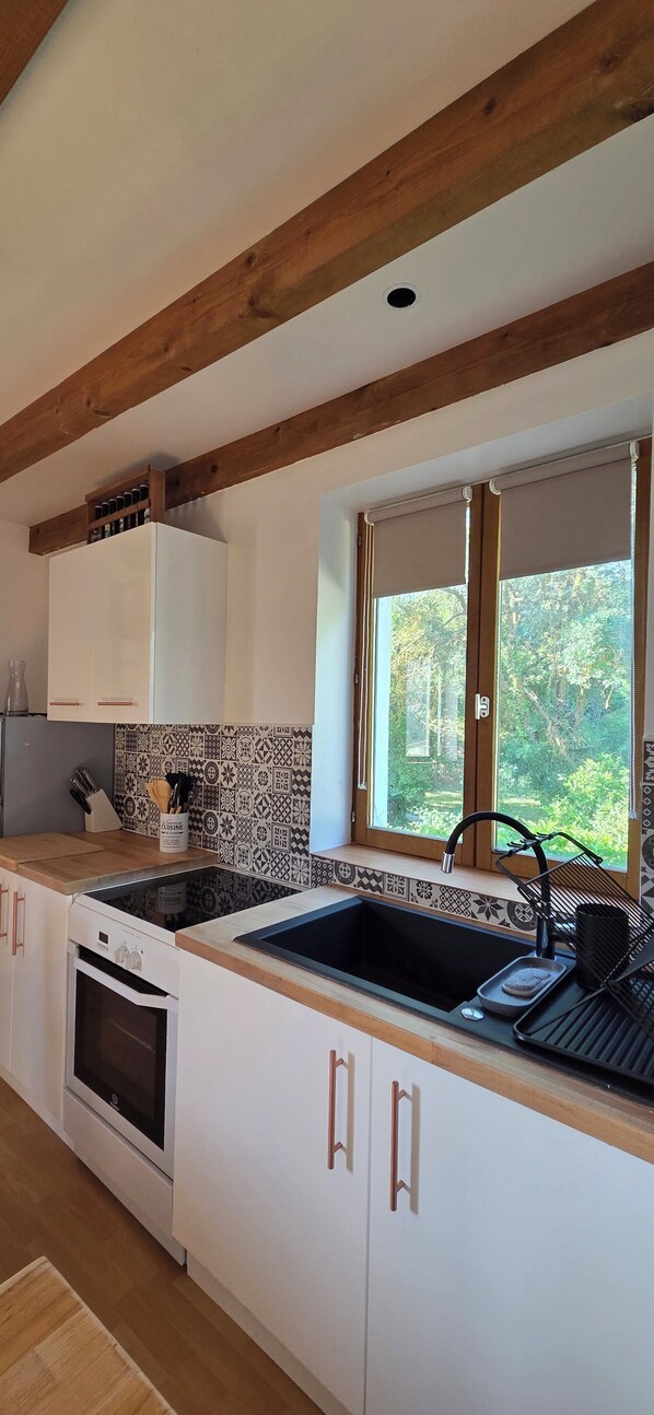 A kitchen with a wooden ceiling, white cabinets, a built-in oven, a sink, and a window with a view of greenery.