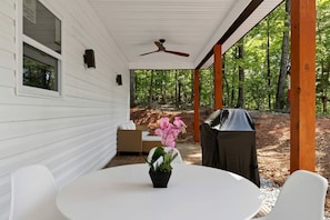 Eine überdachte Terrasse mit Tisch, Stühlen, Deckenventilator und Grill.