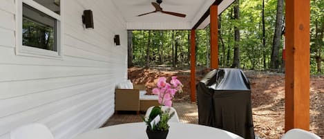 A covered patio with a table, chairs, a ceiling fan, and a grill.