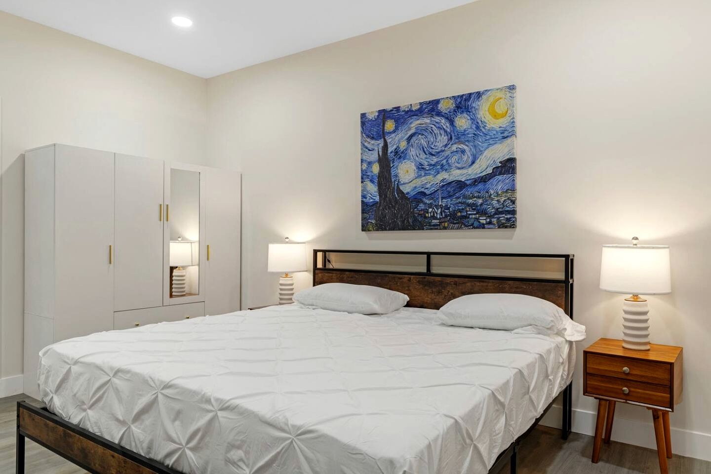 Un dormitorio con cama, lámparas de noche, un armario y un cuadro en la pared.