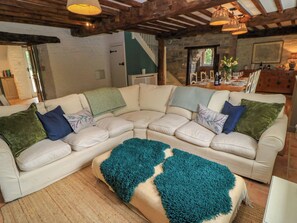 A cozy living room with a sectional sofa, a teal throw blanket, and a dining area with a table set for four. - The Farmhouse (Langport)