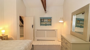 Een slaapkamer met een bed, een kaptafel, een spiegel en een wandplank met foto's.