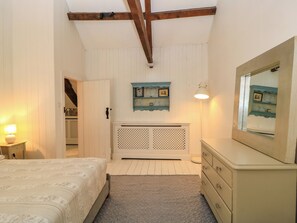 A bedroom with a bed, dresser, mirror, and a wall-mounted shelf with pictures. - The Farmhouse (Langport)