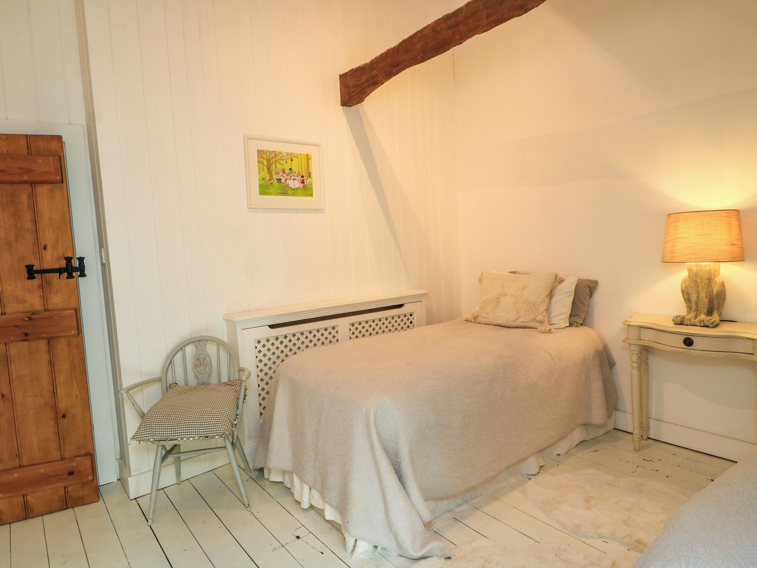 Ein Schlafzimmer mit einem Bett, einem Sessel, einer Holztür, einem Wandbild und einer Nachttischlampe.