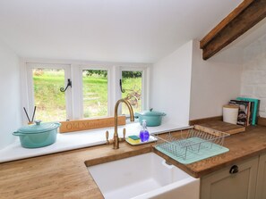 A kitchen with a white sink, wooden countertop, and a window with a view of a garden. - The Farmhouse (Langport)