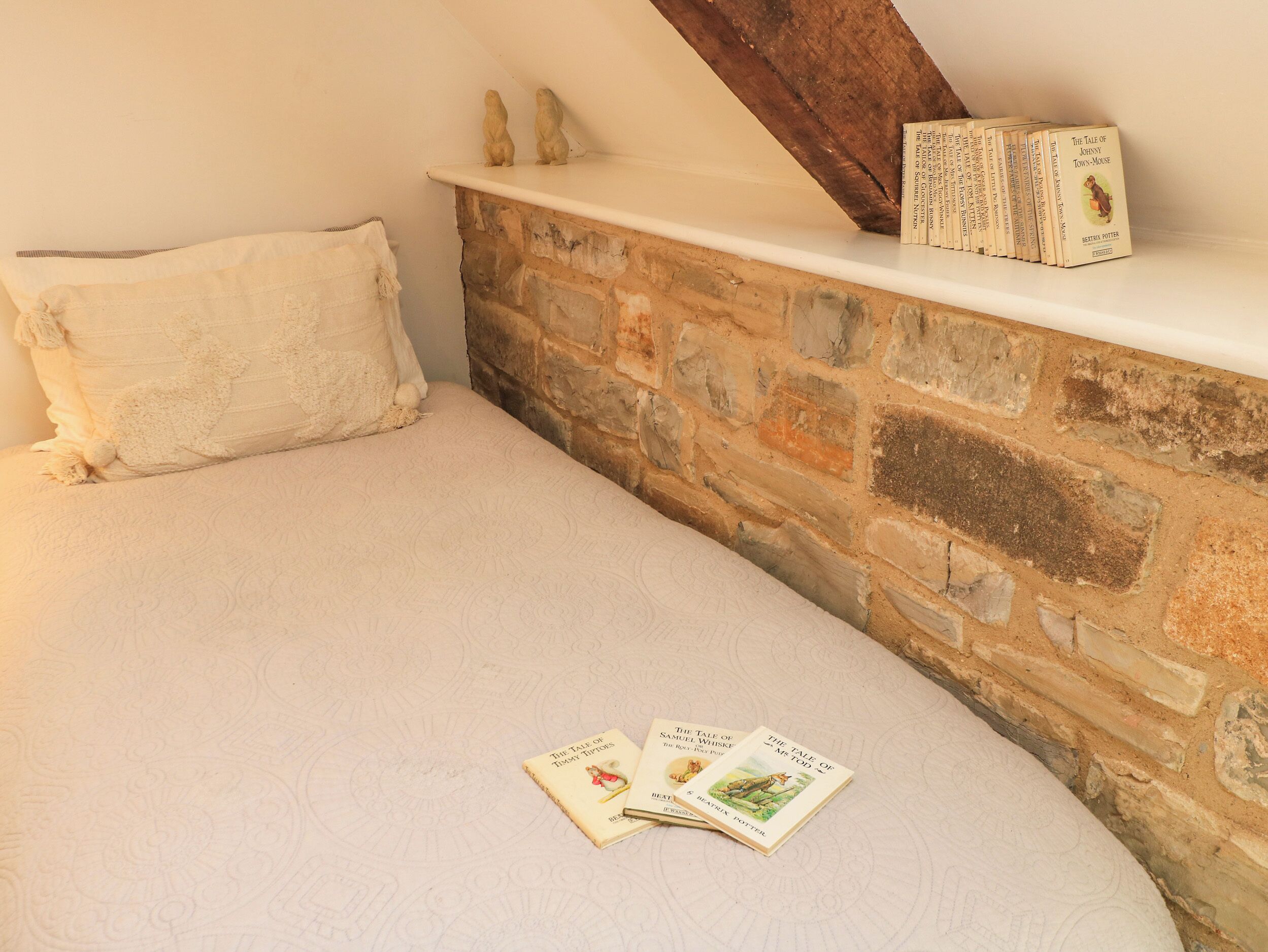 Quarto com parede de pedra, cama branca e estante com livros.