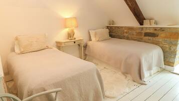 A bedroom with two beds, a nightstand with a lamp, a chair, and a stone wall.