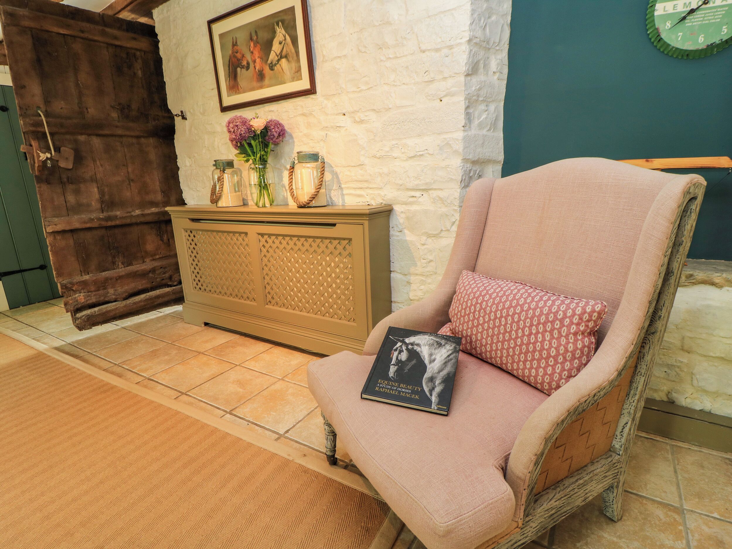 A room with a wicker chair, a book, a vase with flowers, a wooden cabinet, and a door.