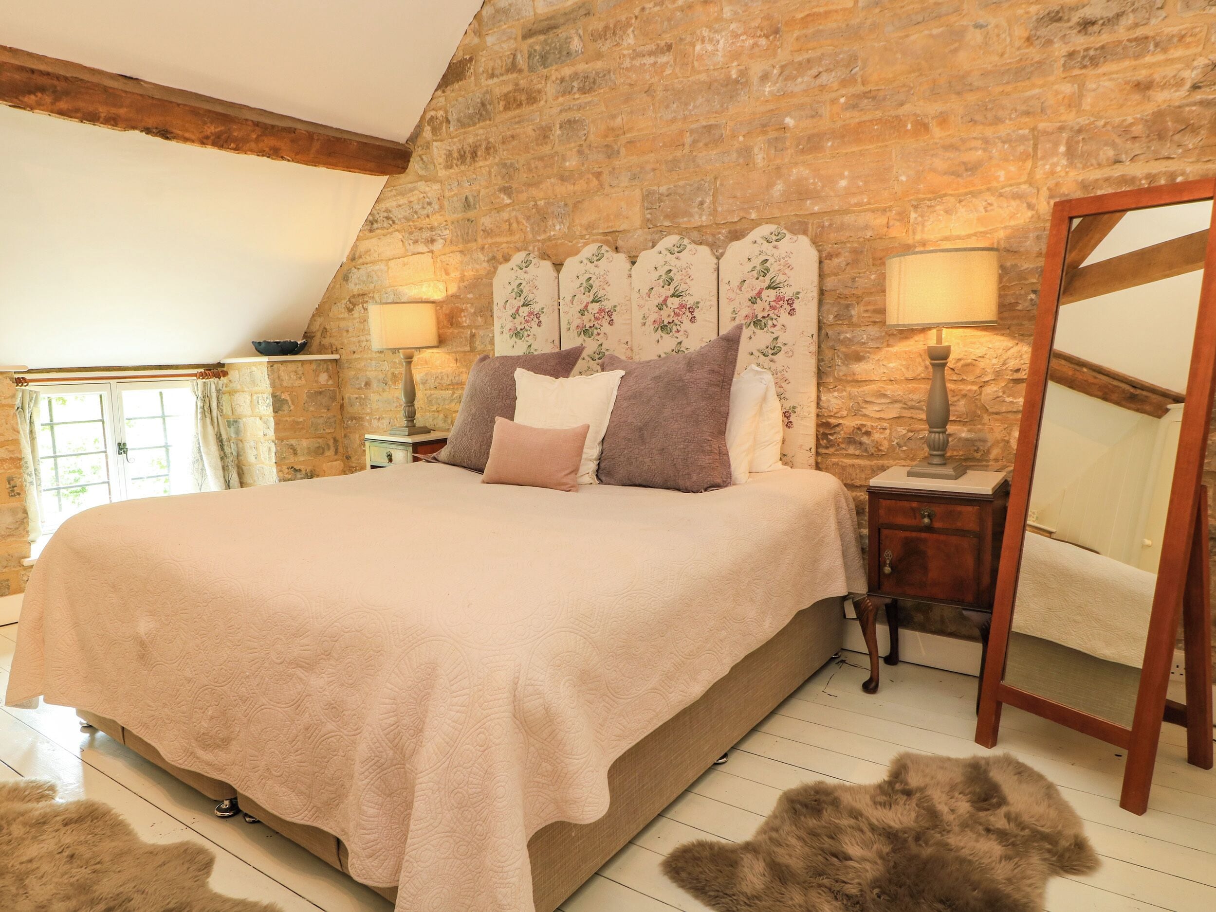 A bedroom with a large bed, a stone wall, a wooden ceiling, and a mirror.
