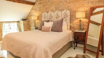 A bedroom with a large bed, a stone wall, a wooden ceiling, and a mirror.
