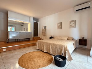 Ein Schlafzimmer mit Bett, Nachttischen, einem Spiegel und einem Badezimmer mit Waschbecken und Waschtisch.