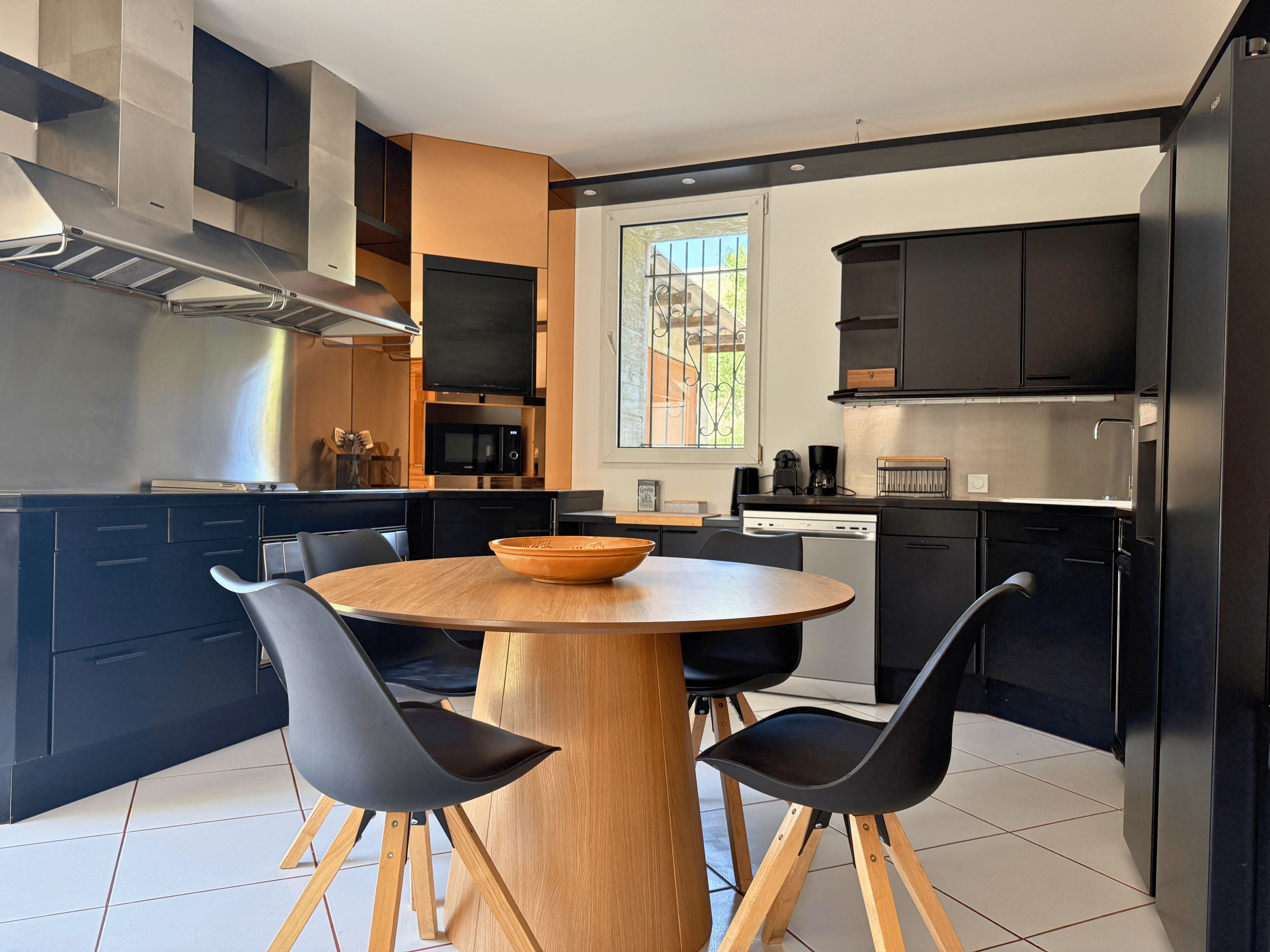 A modern kitchen with black cabinets, a wooden dining table, and black chairs.