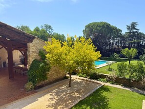 Ein Steinhaus mit einer Pergola, einem Baum und einem Swimmingpool in einem angelegten Garten.