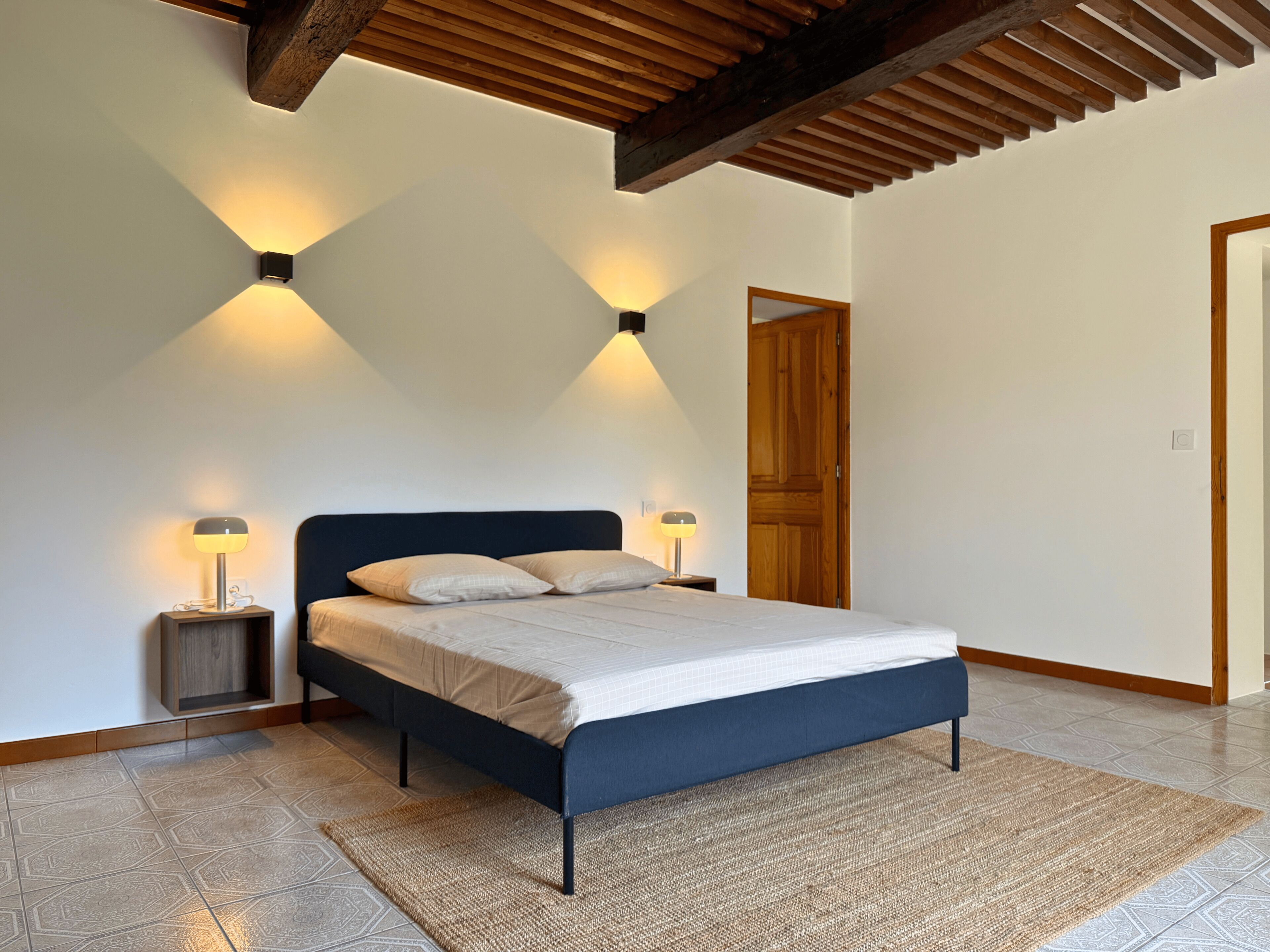 A bedroom with a bed, two bedside lamps, a wooden door, and a sloped ceiling.