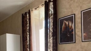 A room with a bed, a white chair, a small table, and curtains.