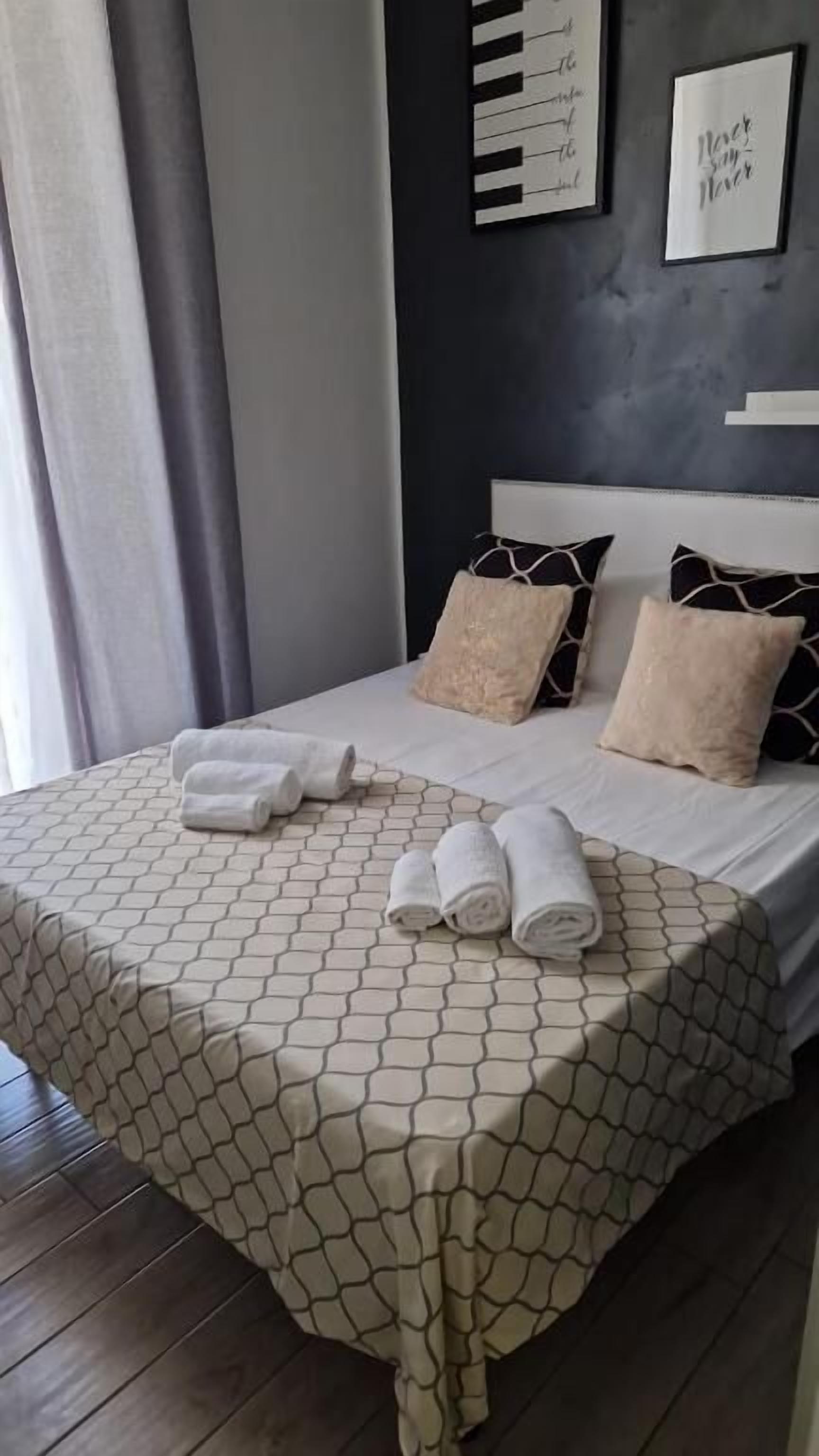 A neatly made bed with a patterned bedspread and pillows, a set of towels on the bed, and a wall with a framed quote.