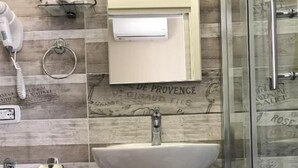 A bathroom with a white sink, a mirror, a telephone, and a shower area.