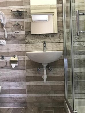 Une salle de bain avec un lavabo blanc, un miroir, un téléphone et un espace douche.