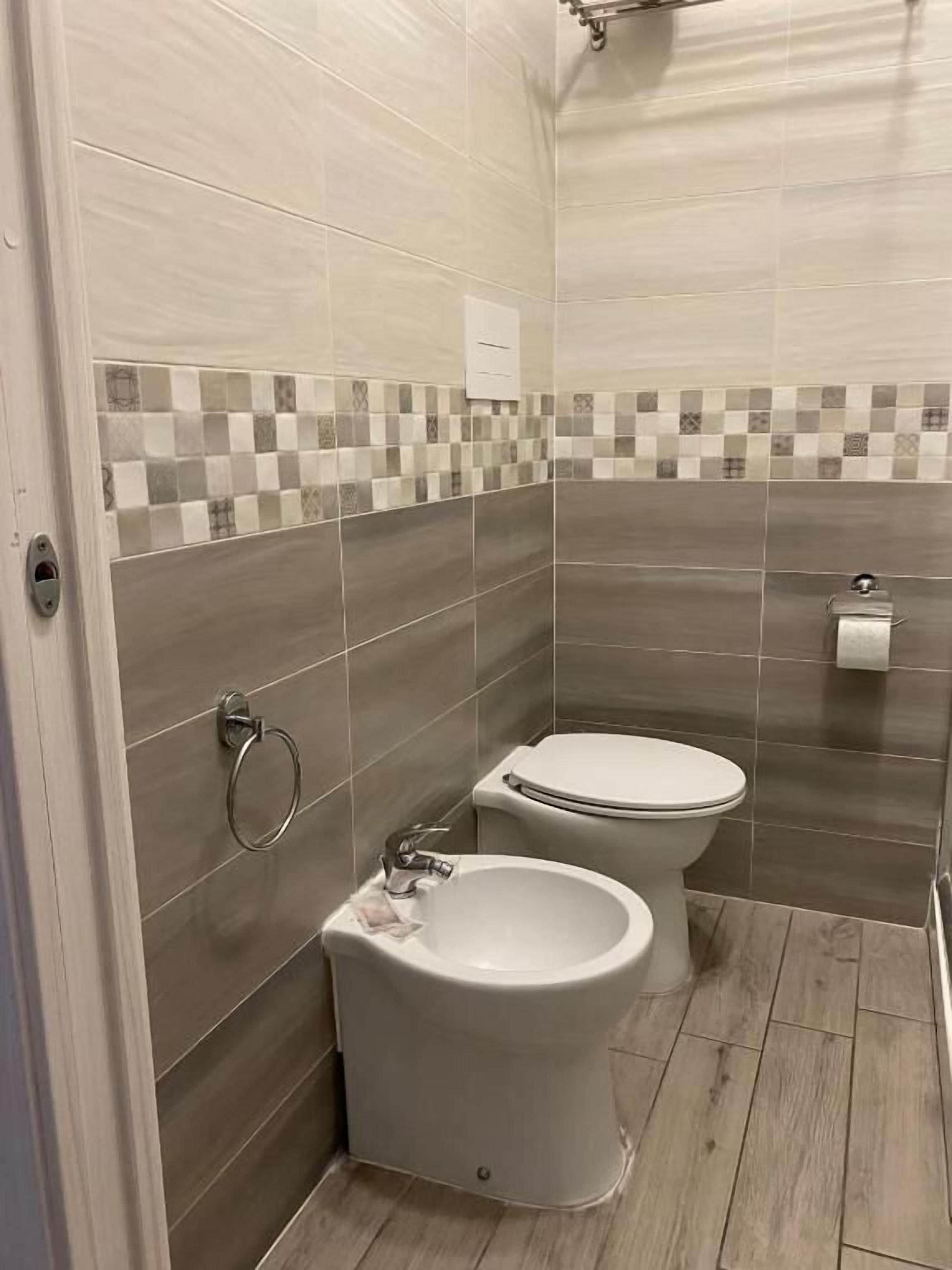 A bathroom with two toilets, a bidet, and a tiled backsplash.