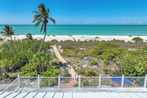 A beach view with a pathway, palm trees, and a white fence. - Beachfront Private Pool Home - Sanibel Shuffle Beach House (Sanibel Island)
