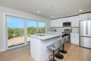 A modern kitchen with a central island, bar stools, white cabinetry, and a view of the outdoors. - Beachfront Private Pool Home - Sanibel Shuffle Beach House (Sanibel Island)