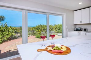 Cozinha com bancada de mármore, tábua de madeira com queijo e azeitonas, e duas taças de vinho tinto.