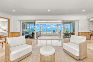 A modern living room with wicker furniture, a glass door leading to a balcony with a view of the ocean. - NEW! Ibis Cottage | Direct Beachfront Retreat on Manasota Key (Englewood)
