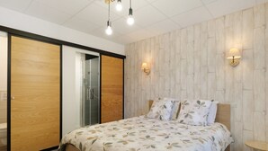 A bedroom with a bed, wooden wardrobe, and two wall-mounted lamps.
