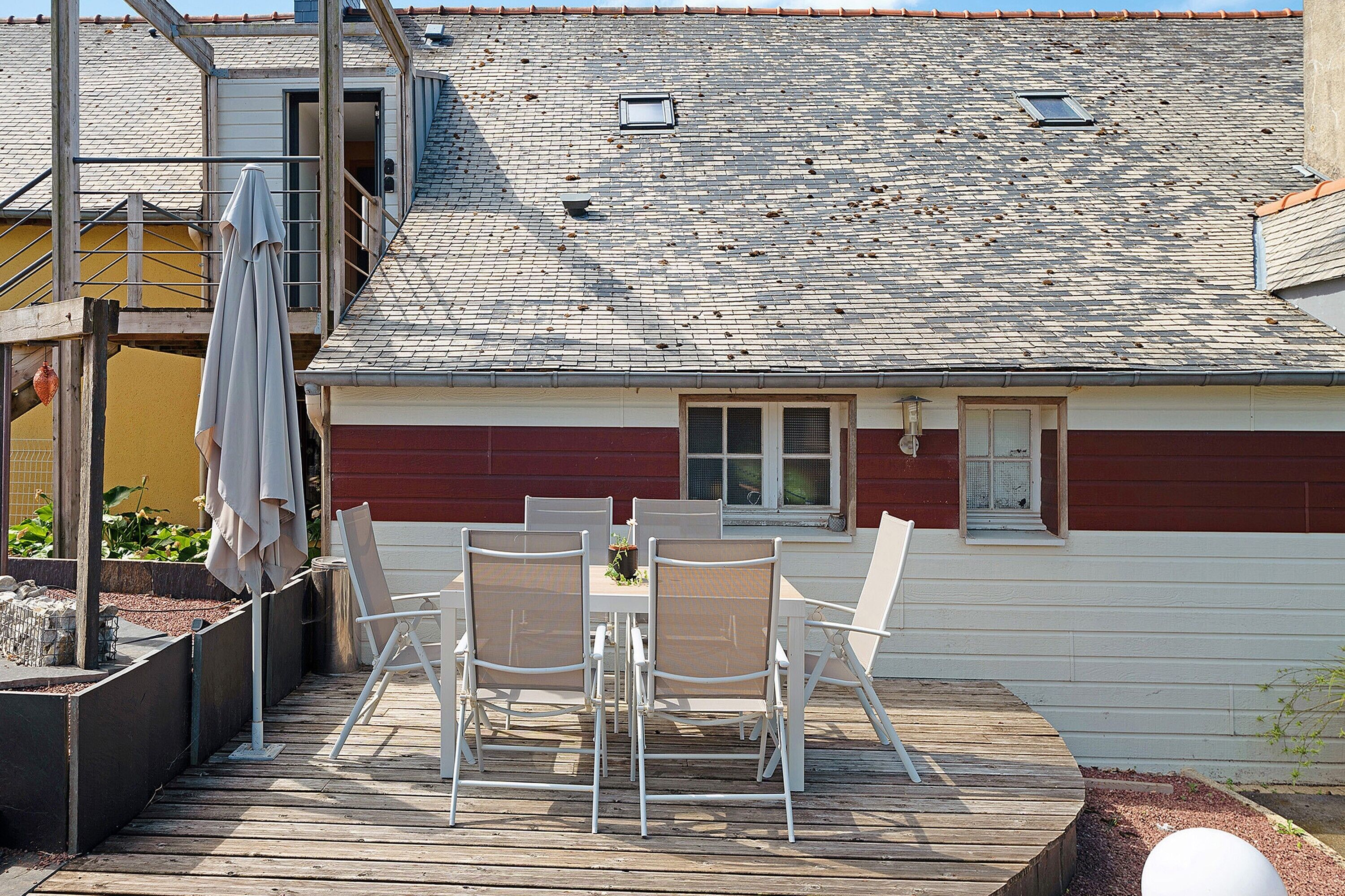 A deck with outdoor furniture, a window with shutters, and a red building in the background.