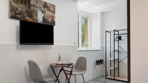 A hotel room with a flat-screen TV, two chairs, a small table, a window with a view, and a coat rack. - Guest Room “L'Horizon” with Shared Terrace, Shared Garden and Wi-Fi (Romillé)