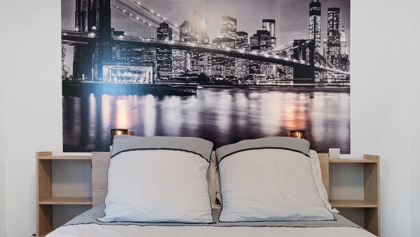 A bed with two pillows, a nightstand, and a cityscape poster on the wall. - Guest Room “L'Horizon” with Shared Terrace, Shared Garden and Wi-Fi (Romillé)