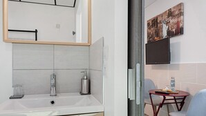 A modern bathroom with a sink, mirror, and a small table with chairs. - Guest Room “L'Horizon” with Shared Terrace, Shared Garden and Wi-Fi (Romillé)