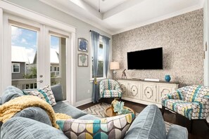Ein Wohnzimmer mit großem Fenster, Flachbildfernseher, gemusterten Sofas und einer Wandverkleidung.