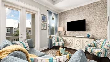 Een woonkamer met een groot raam, een flatscreen televisie, gestreepte banken en een decoratieve wand.